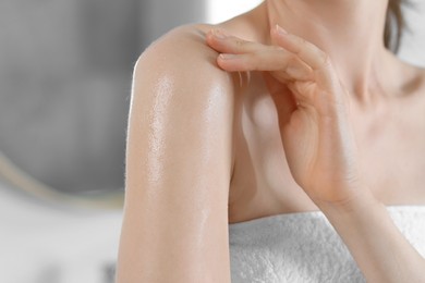 Photo of Woman applying body oil onto shoulder in bathroom, closeup