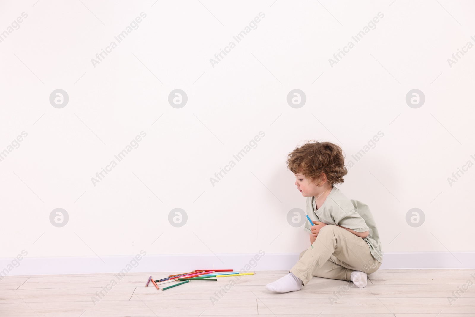 Photo of Little boy with colorful pencils near white wall indoors. Space for text