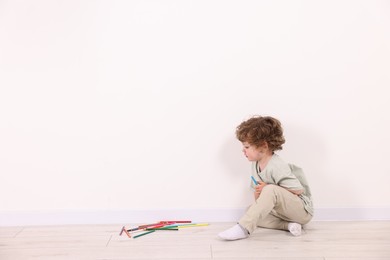 Photo of Little boy with colorful pencils near white wall indoors. Space for text