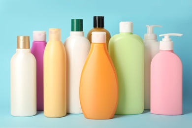 Bottles with different hair care cosmetics on light blue background