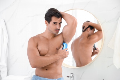 Photo of Handsome young man applying deodorant in bathroom