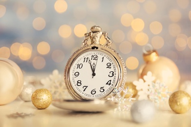 Photo of Pocket watch and festive decor on table against blurred lights. New Year countdown