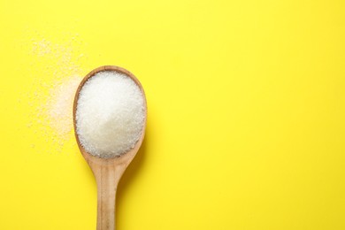 Photo of Granulated sugar in spoon on yellow background,top view. Space for text