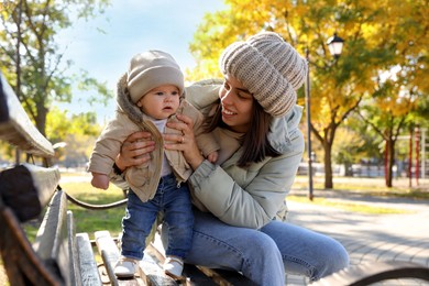 Happy mother with her baby son on bench in autumn park
