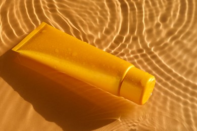 Photo of Tube with moisturizing cream in water on orange background