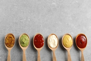 Photo of Wooden spoons with different sauces and space for text on gray background, flat lay