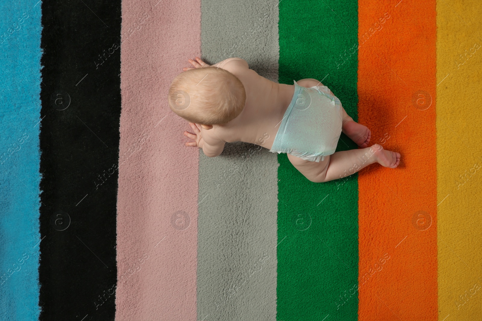 Photo of Cute little baby crawling on colorful carpet indoors, top view