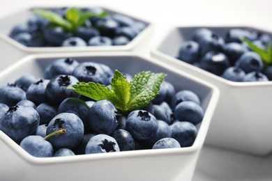 Photo of Fresh blueberries with green leaves in white dishware, closeup