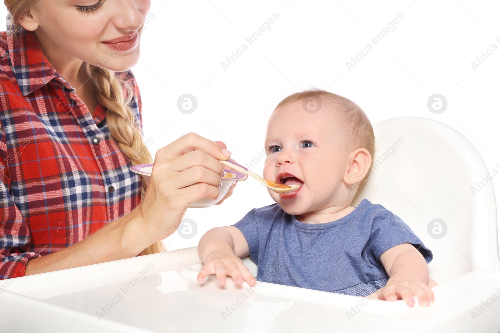 Photo of Woman feeding her child in highchair against white background. Healthy baby food