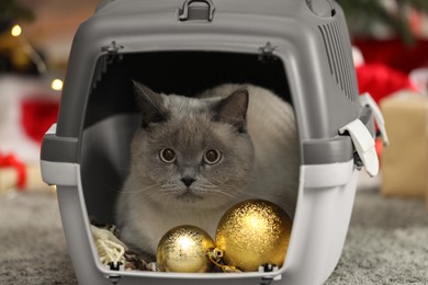 Cute cat in pet carrier near Christmas decor and gift boxes at home
