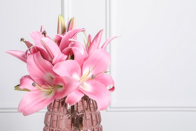 Photo of Beautiful pink lily flowers in vase against white wall, space for text