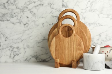 Photo of Wooden cutting boards and mortar with pestle on white table near marble wall, space for text