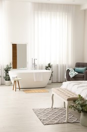 Photo of Stylish light apartment interior with white bathtub and bed