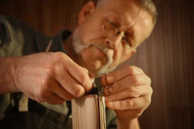 Photo of Man sewing piece of leather in workshop, closeup