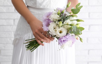 Bride holding beautiful bouquet with Eustoma flowers near brick wall, closeup