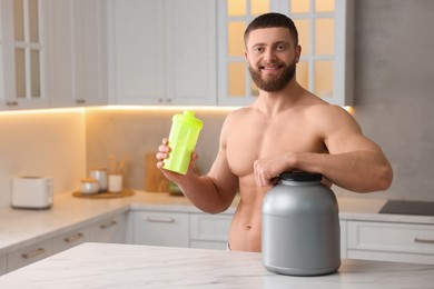 Young man with shaker of protein and powder at white marble table in kitchen, space for text