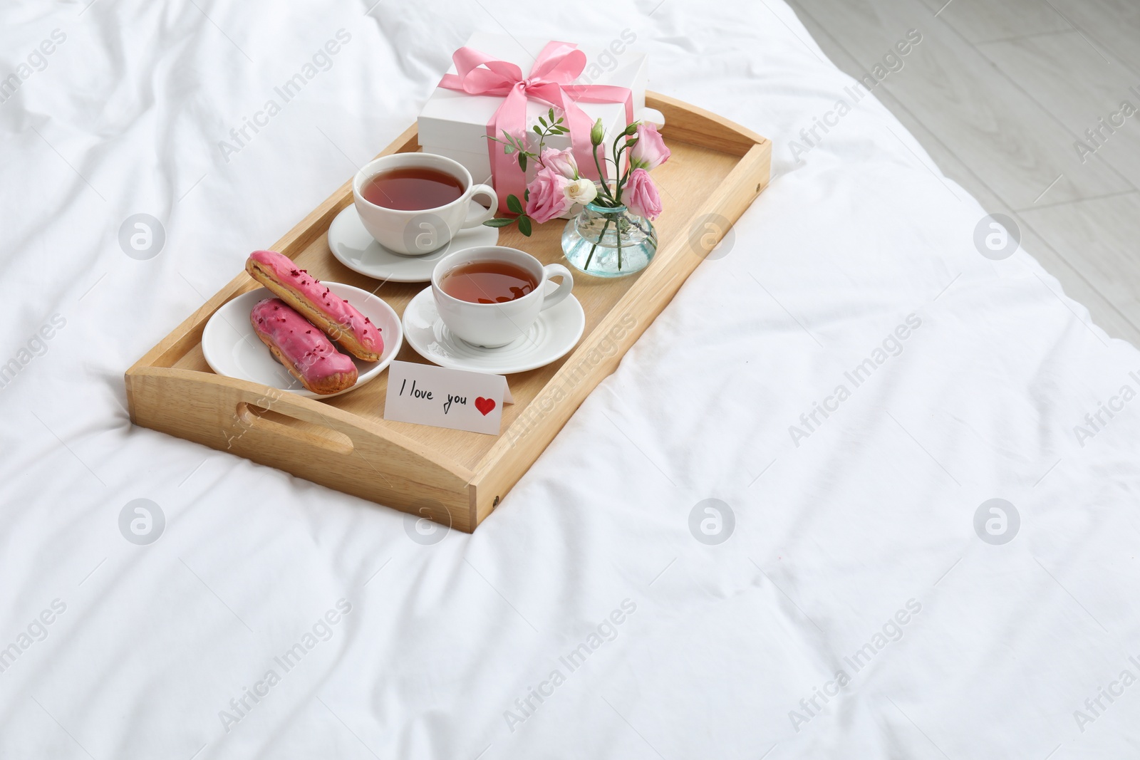 Photo of Tasty breakfast served in bed. Delicious eclairs, tea, gift box, flowers and card with phrase I Love You on tray, space for text