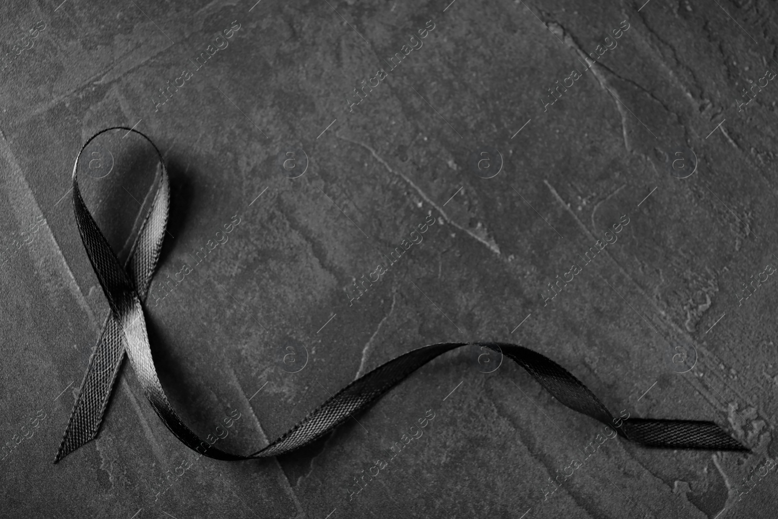 Photo of Black ribbon on dark grey stone surface, top view with space for text. Funeral symbol