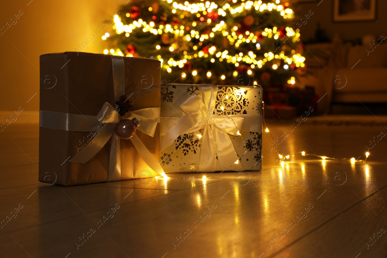 Photo of Beautiful gift boxes against fir tree with Christmas lights at home