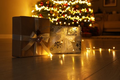 Beautiful gift boxes against fir tree with Christmas lights at home