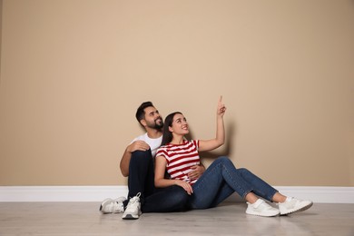 Photo of Young couple sitting on floor near beige wall indoors