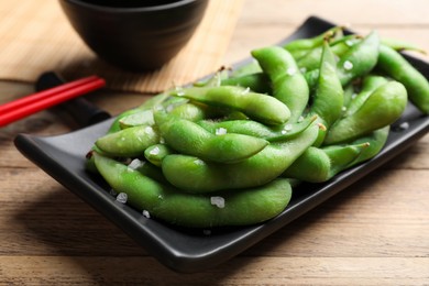 Photo of Black plate with green edamame beans in pods on wooden table