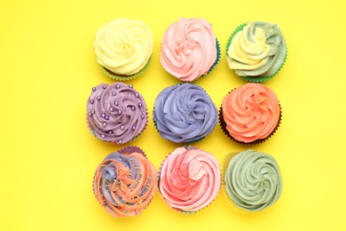 Photo of Delicious cupcake with bright cream on yellow background, flat lay