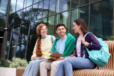Photo of Happy young students studying with notebooks on bench outdoors