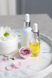 Bottles of cosmetic serum, cream jar and flowers on table, closeup
