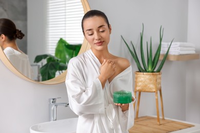 Photo of Young woman applying aloe gel onto her skin in bathroom