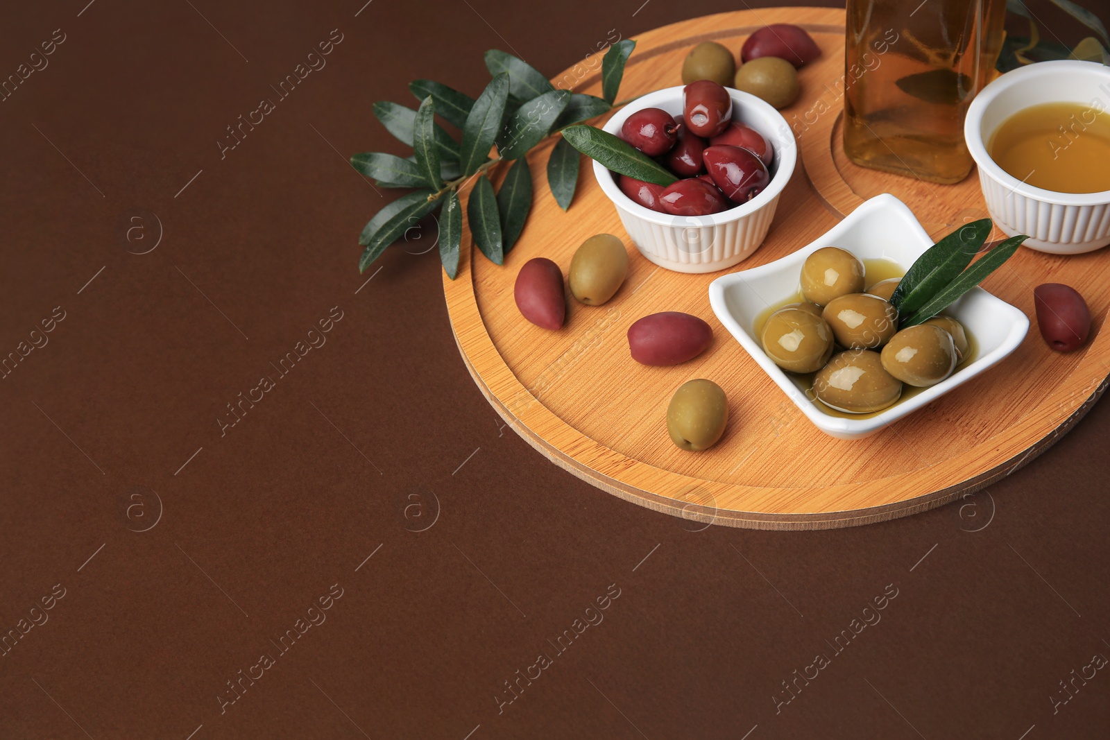 Photo of Oil, olives and tree twig on brown table, space for text
