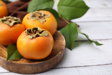 Delicious ripe juicy persimmons on white wooden table, closeup. Space for text