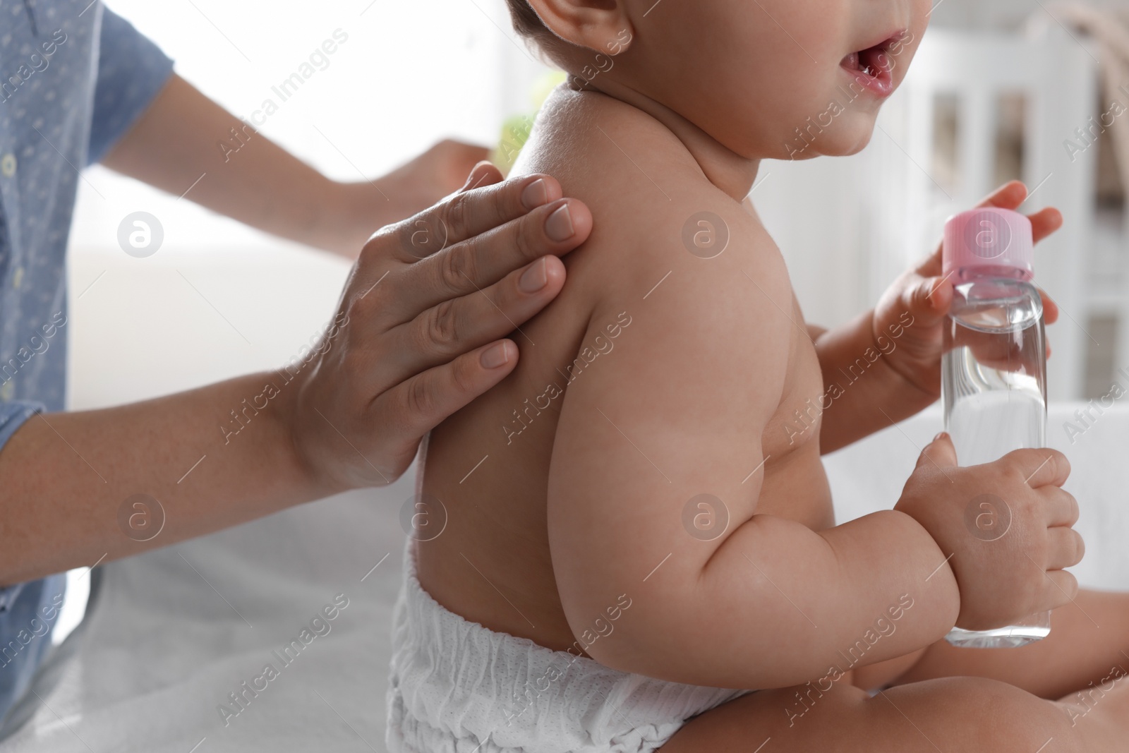 Photo of Mother massaging her baby with oil on changing table at home, closeup