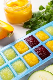 Photo of Different purees in ice cube tray and ingredients on white table, closeup. Ready for freezing