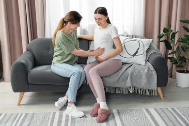 Doula taking care of pregnant woman on sofa at home. Preparation for child birth