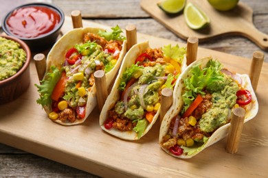 Delicious tacos with guacamole, meat and vegetables served on wooden table, closeup