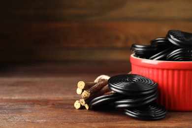 Tasty black candies and dried sticks of liquorice root on wooden table, closeup. Space for text