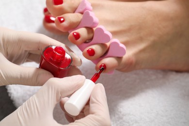 Pedicurist painting client`s toenails with red polish in beauty salon, closeup