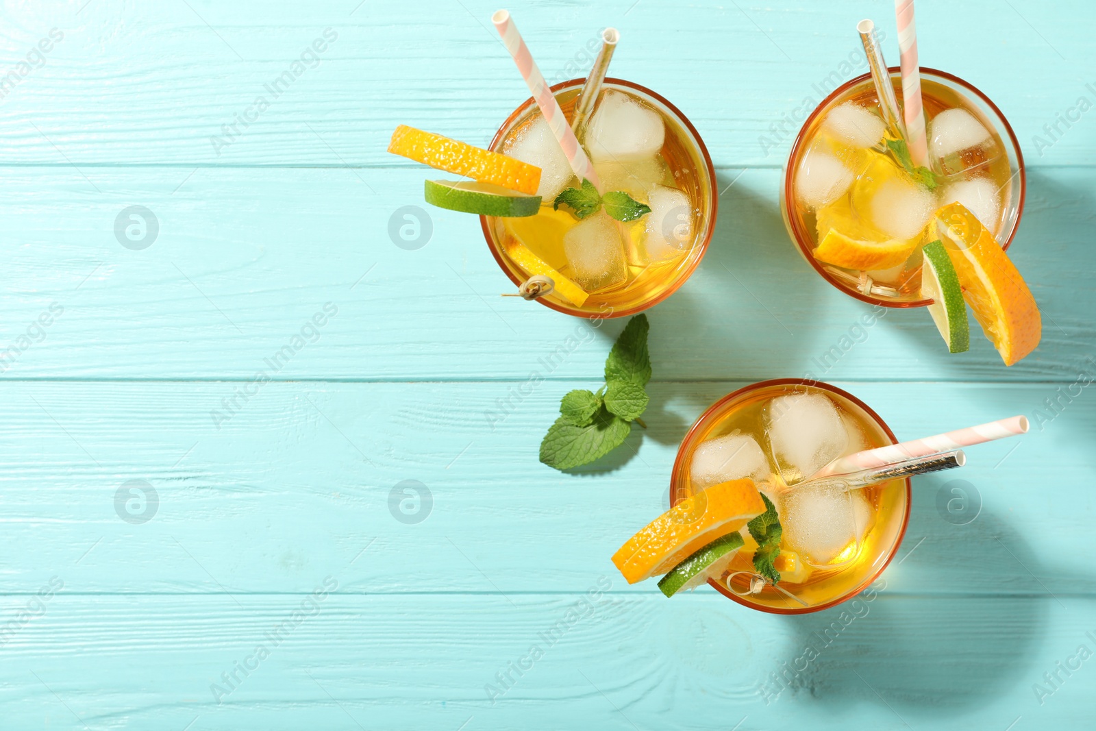 Photo of Delicious refreshing drink with orange and lime slices on light blue wooden table, flat lay. Space for text