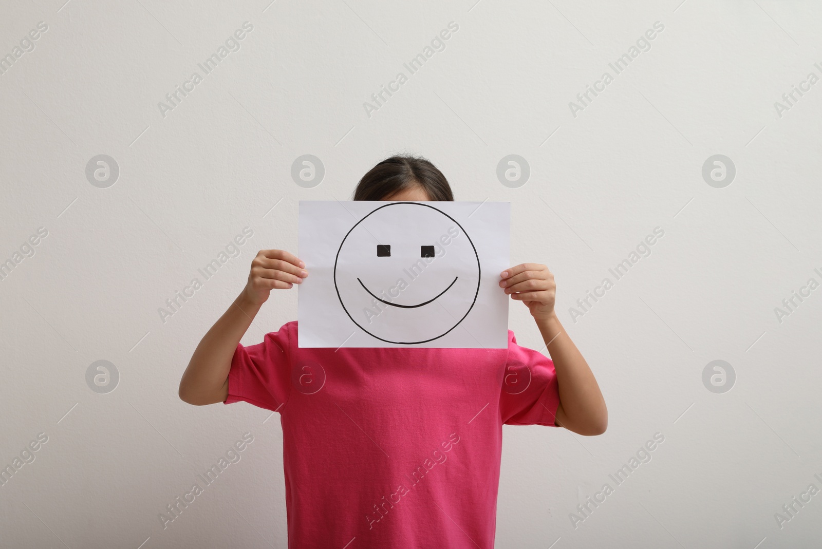 Photo of Little girl hiding behind sheet of paper with happy face on white background
