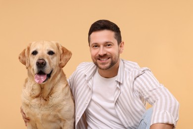 Photo of Man hugging with adorable Labrador Retriever dog on beige background. Lovely pet