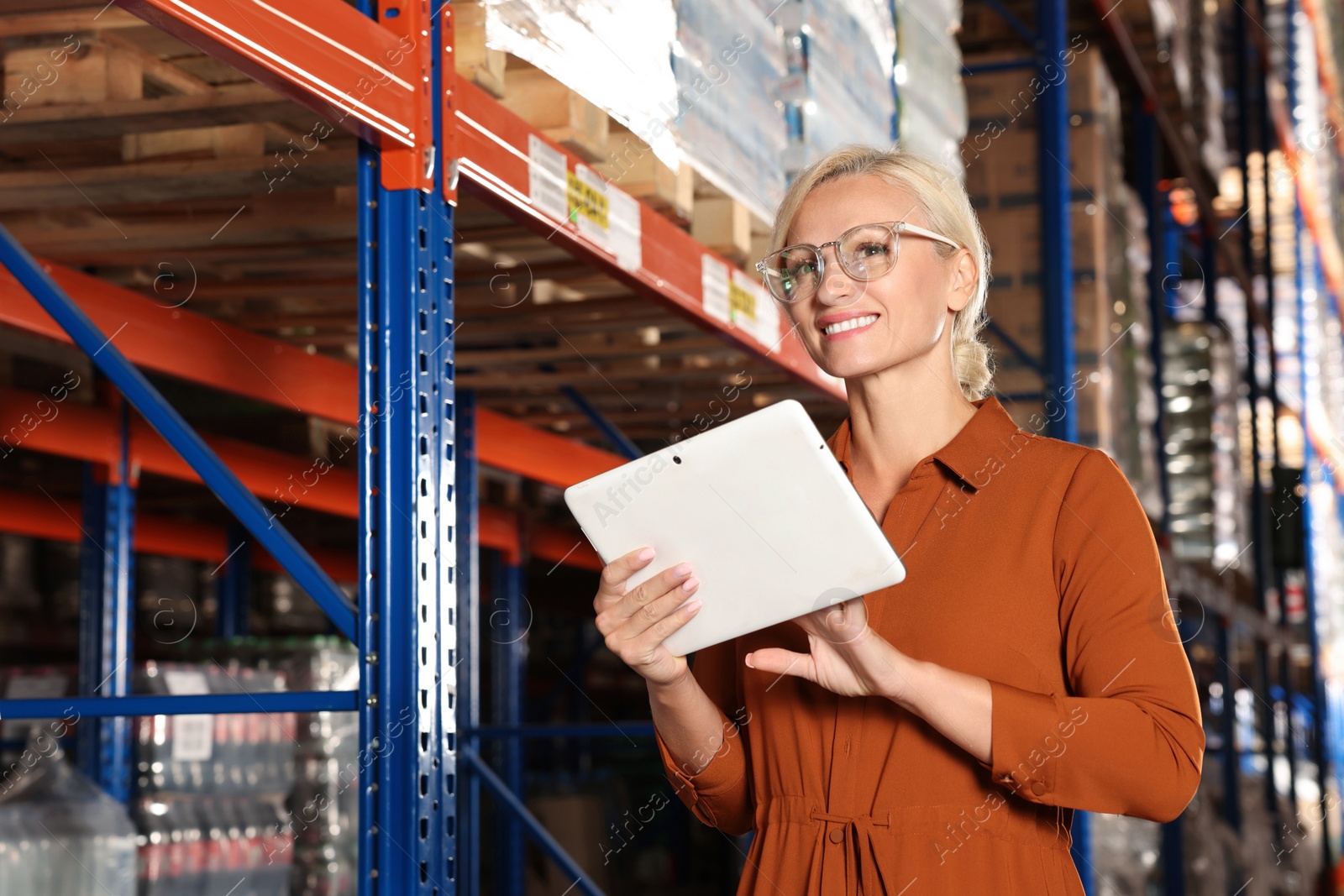 Photo of Happy manager using modern tablet in warehouse with lots of products