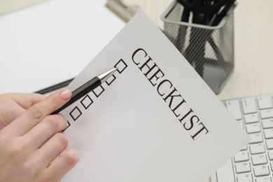 Photo of Woman filling Checklist with pen at workplace, closeup