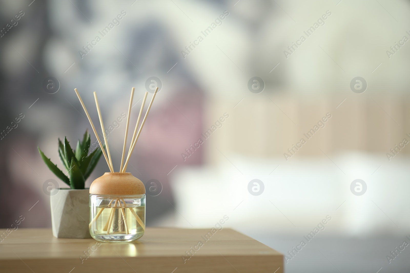 Photo of Aromatic reed air freshener and houseplant on table indoors. Space for text