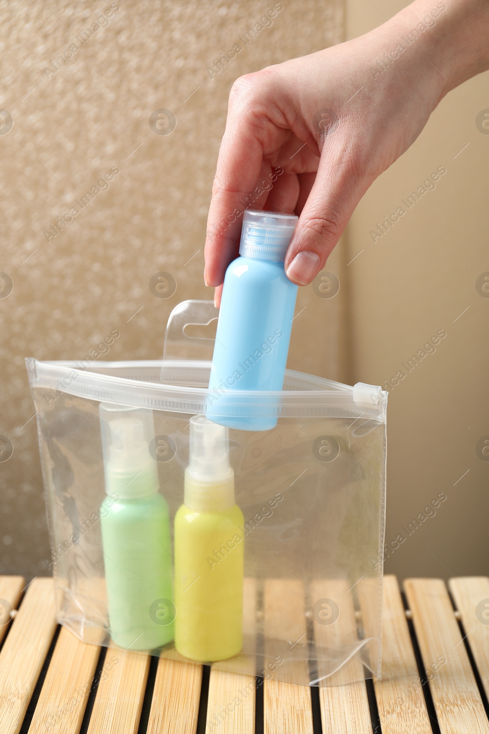 Photo of Woman packing cosmetic travel kit at wooden table, closeup. Bath accessories