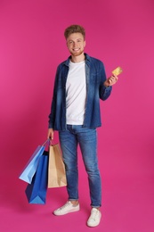 Photo of Young man with credit card and shopping bags on color background. Spending money