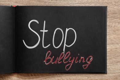 Text Stop Bullying written in black notebook on wooden table, top view