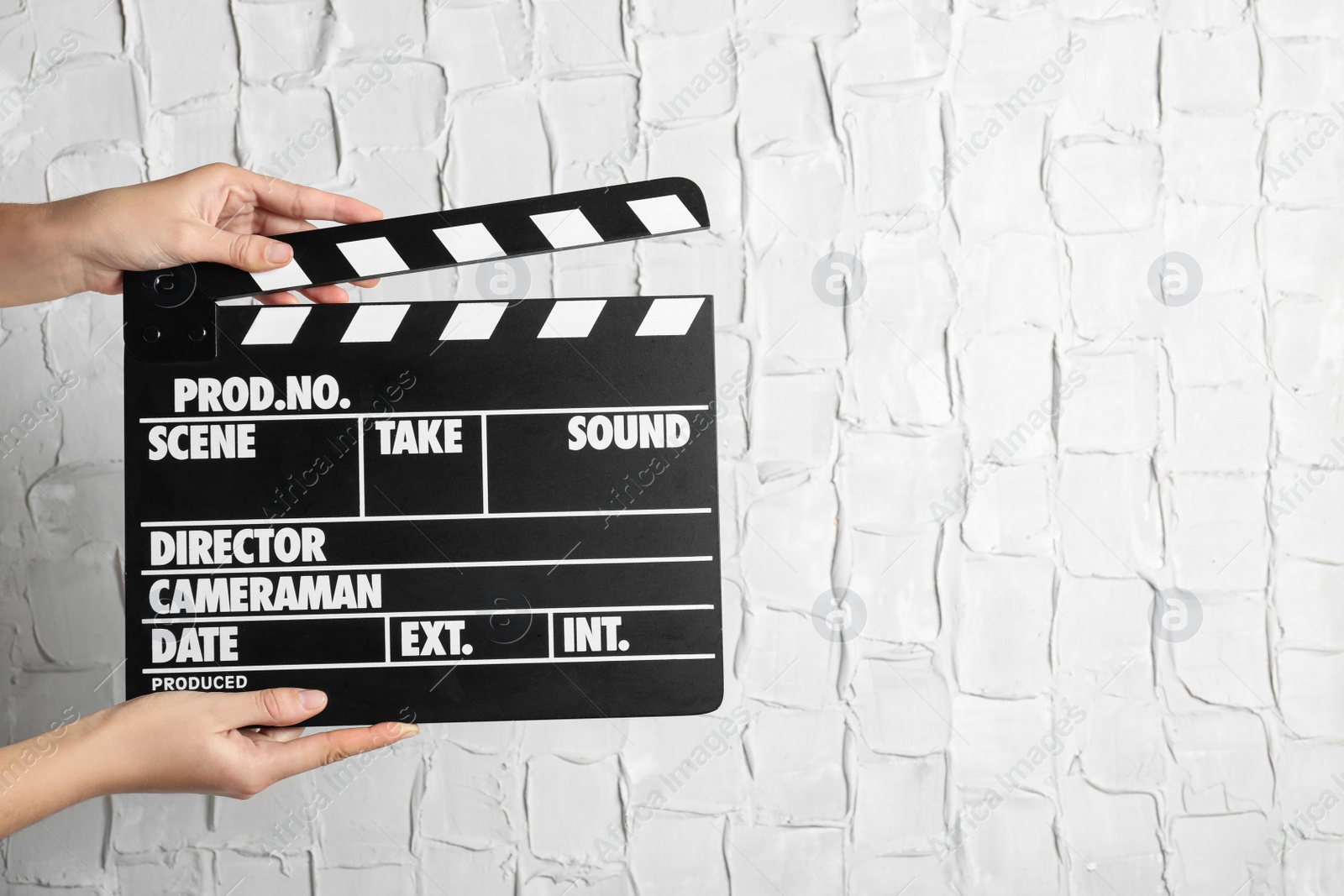 Photo of Woman holding clapperboard against white textured wall, closeup with space for text. Cinema production