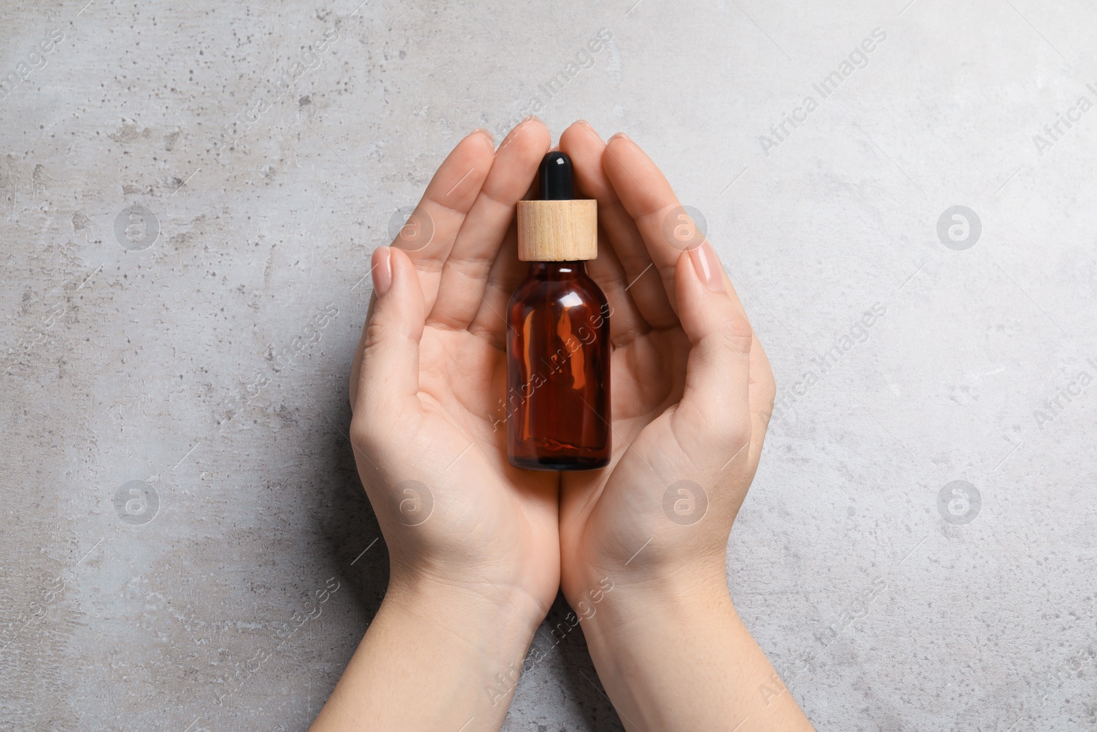 Photo of Woman holding bottle with serum at grey table, top view