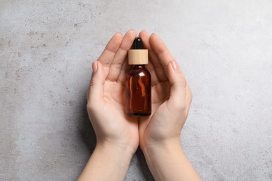Photo of Woman holding bottle with serum at grey table, top view